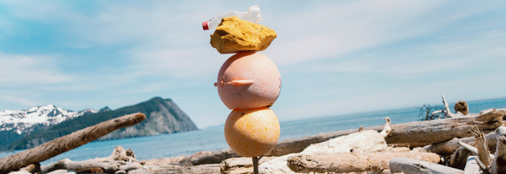 Gore Point Beach Alaska, 2013 A photographic artwork by Andy Hughes show plastic flotsam and jetsam stacked vertically on a stake of driftwood with a dramatic ocean landscape in the background.