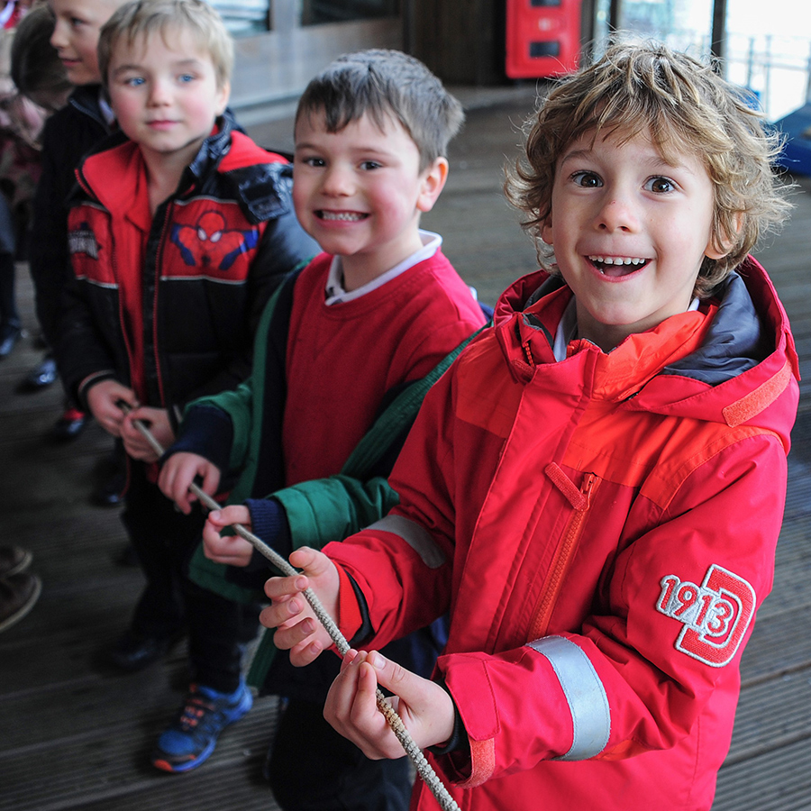 Three children are smiling at the camera taking part in a workshop where they are holding a rope.