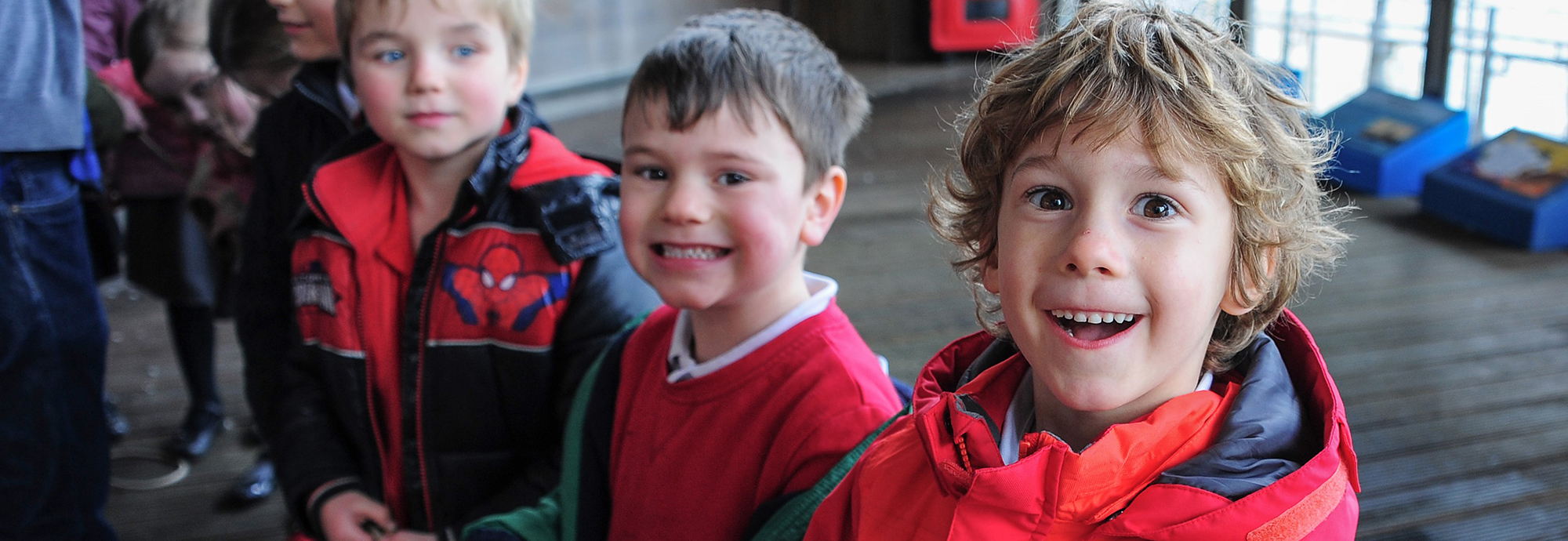 Three children are smiling at the camera taking part in a workshop where they are holding a rope.