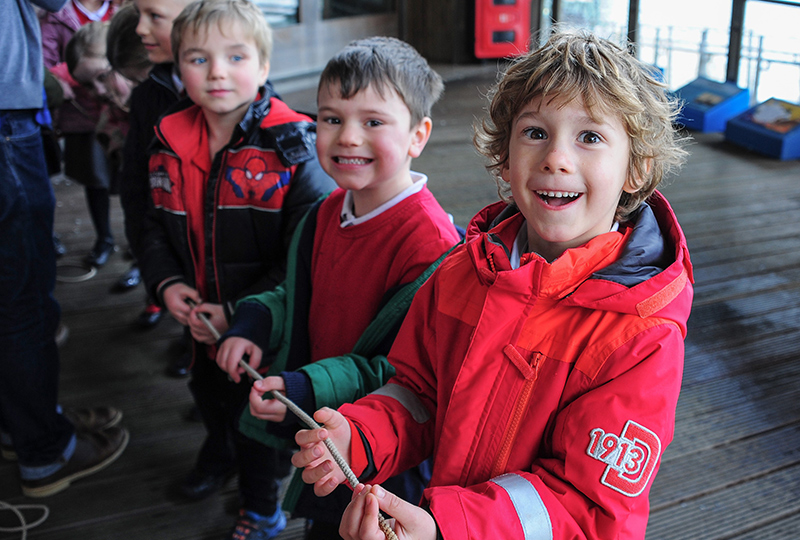 Three children are smiling at the camera taking part in a workshop where they are holding a rope.