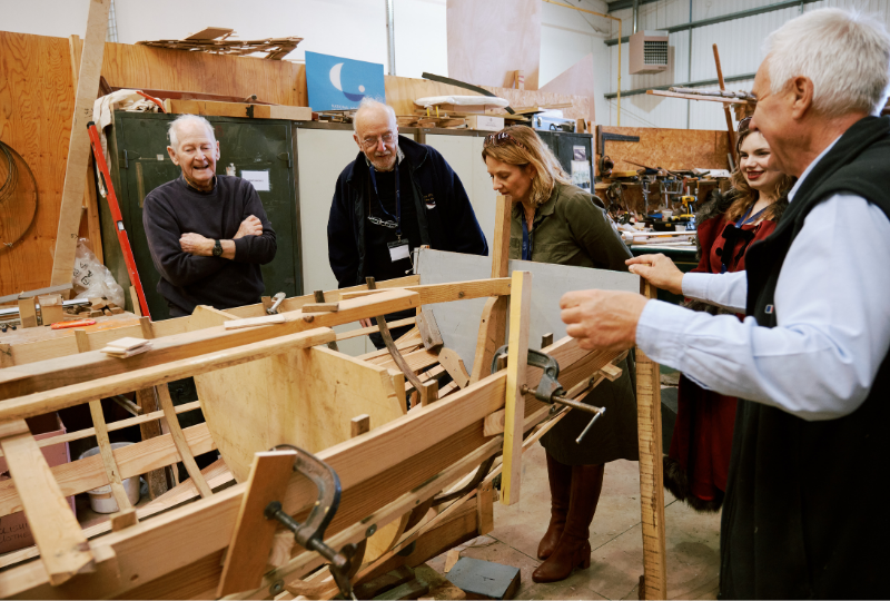 Visitors examine a boatbuilding project in progress as Museum volunteers involved in the build look on.