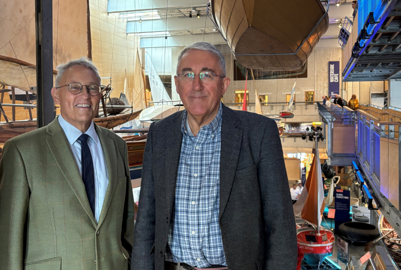 Two men, NMMC Director Richard Doughty and NMMC Board Chair Dr Patrick Newberry, stand side-by-side in the Boat Hall of National Maritime Museum Cornwall.