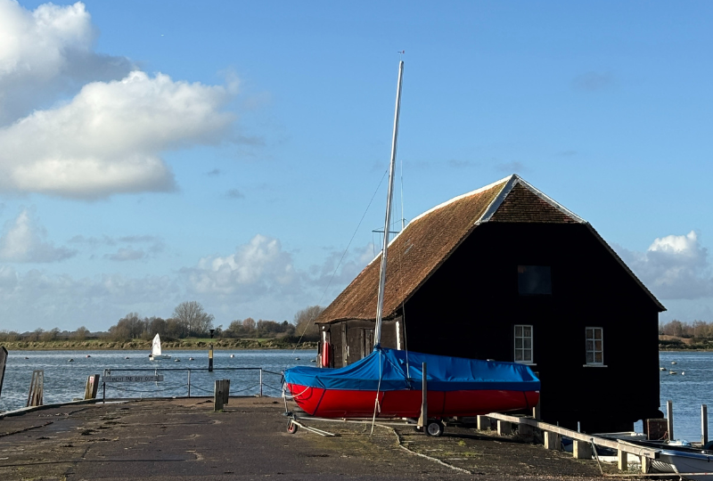 1962 wooden Wayfarer Eleana under a cover at the water's edge.