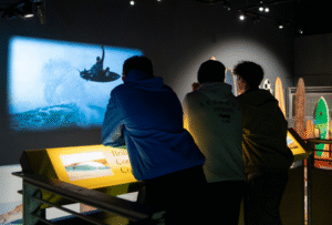Three Museum visitors look at a projected photograph of a surfer in the SURF! Exhibition at National Maritime Museum Cornwall