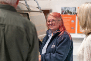 A Museum volunteer smiles and talks to two Museum visitors.