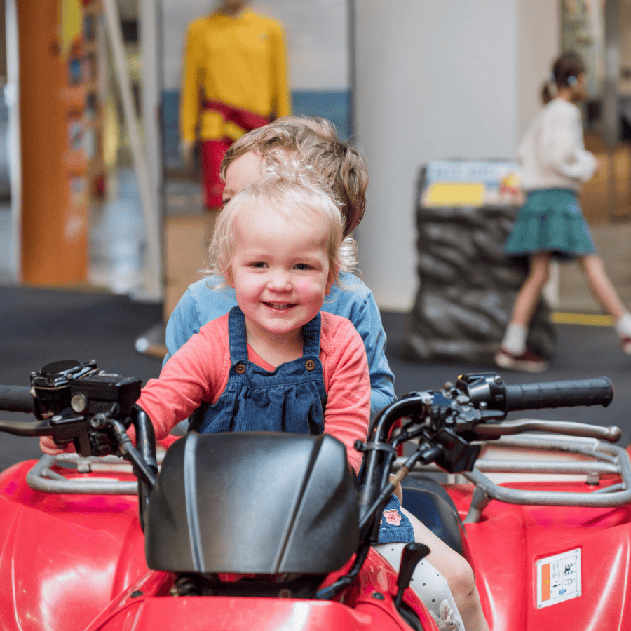 A child smiles having fun sitting on an RNLI Rescue Quad Bike in the RNLI Rescue Zone inside National Maritime Museum Cornwall.