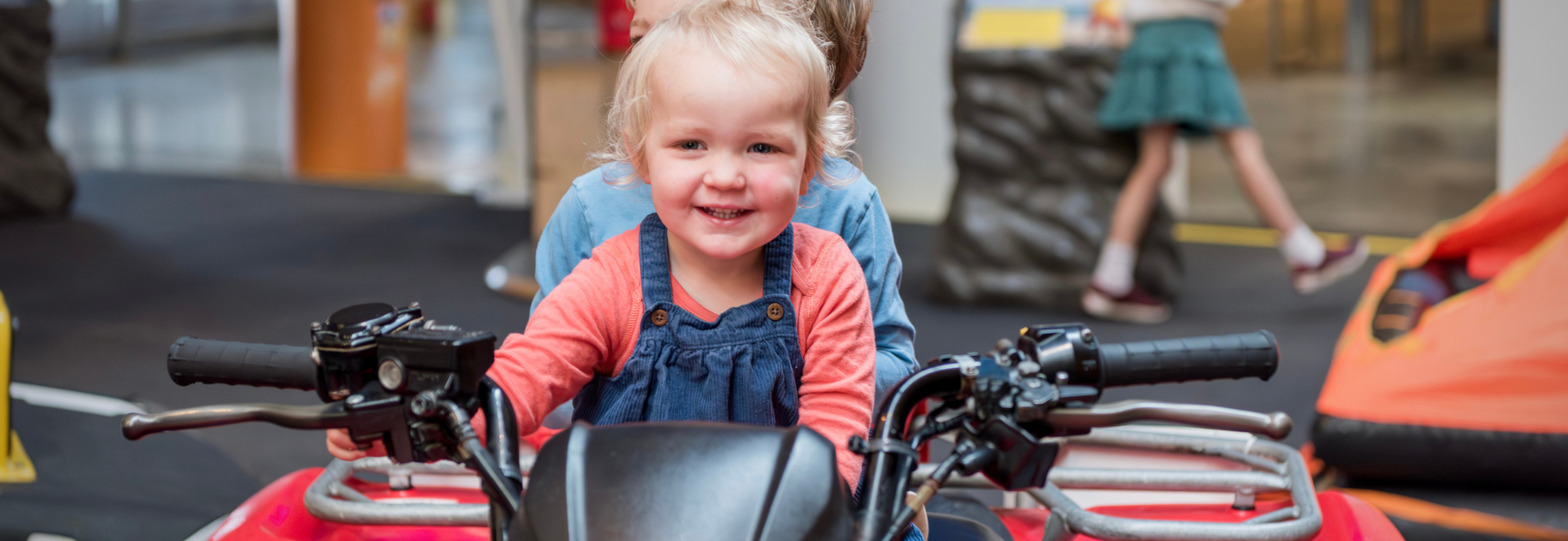 A child smiles having fun sitting on an RNLI Rescue Quad Bike in the RNLI Rescue Zone inside National Maritime Museum Cornwall.