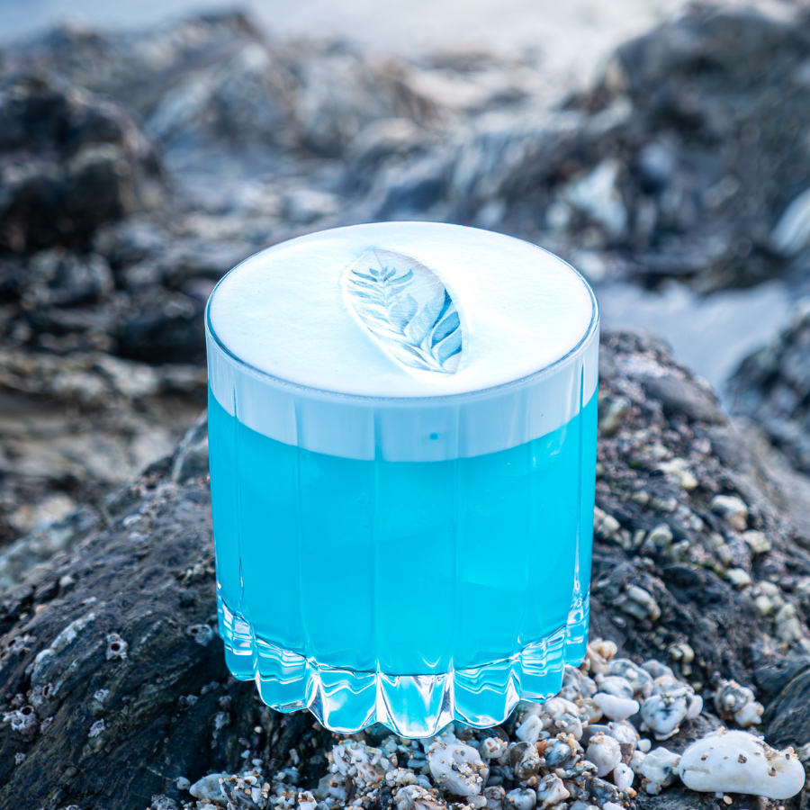 A bright blue cocktail drink with a decorative surfboard design.
