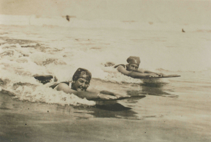 Archive photograph of two women riding bellyboards in the surf