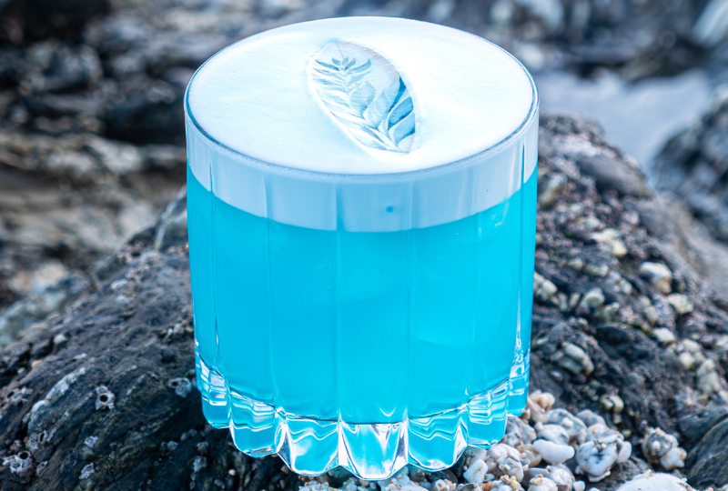 A bright blue cocktail drink with a decorative surfboard design.