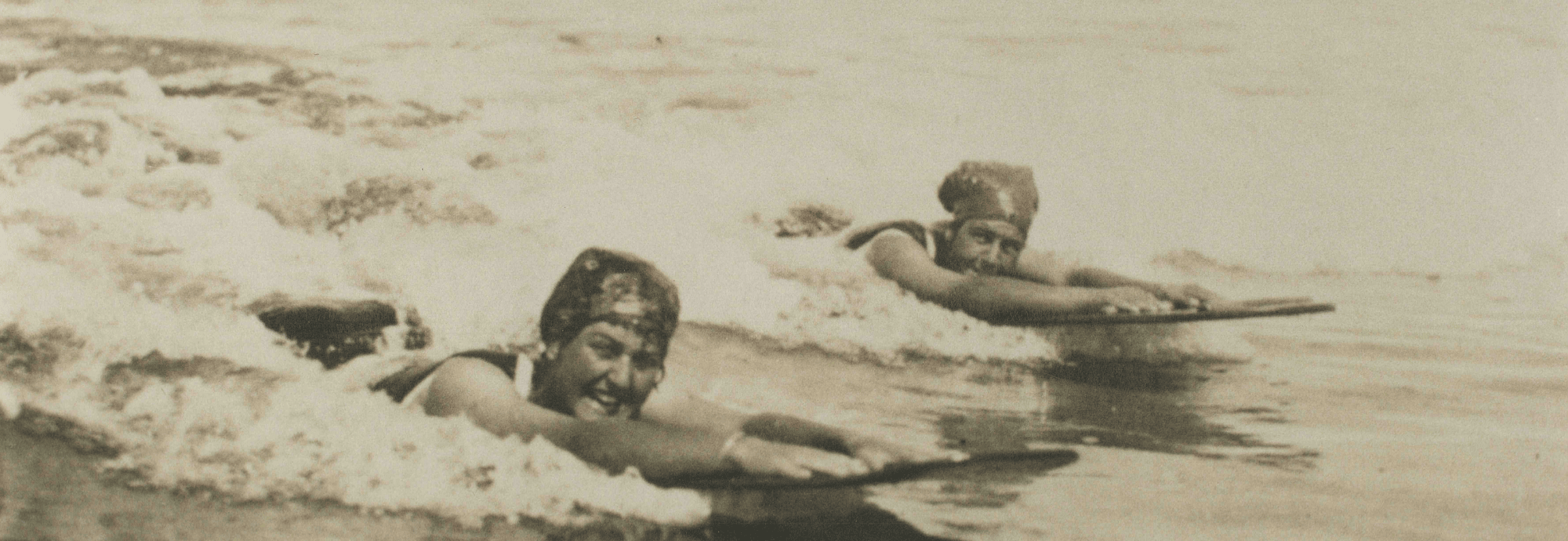 Archive photograph of two women riding bellyboards in the surf