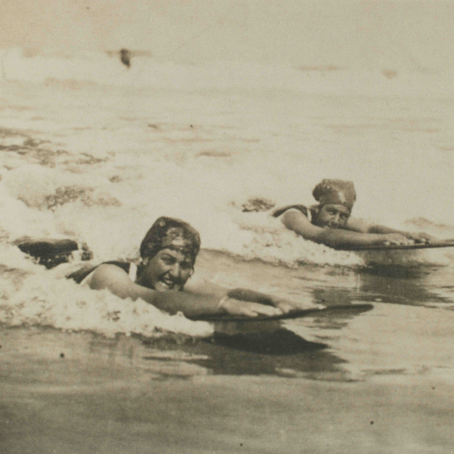 Archive photograph of two women riding bellyboards in the surf