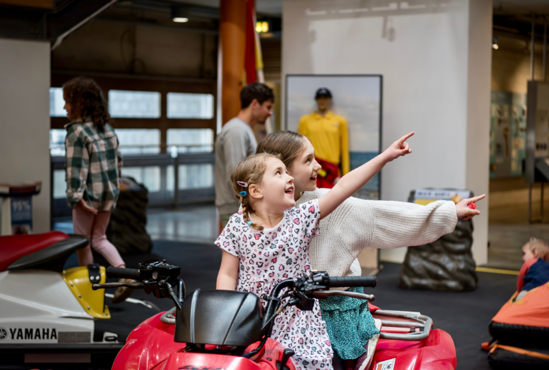 Two children sit on a quadbike display in RNLI Rescue Zone at National Maritime Museum Cornwall.