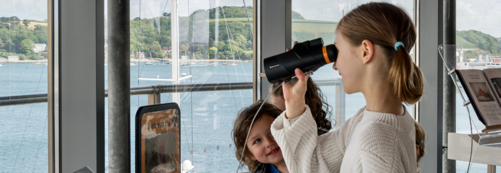 Children look through handheld telescopes to admire the view in The Lookout at National Maritime Museum Cornwall